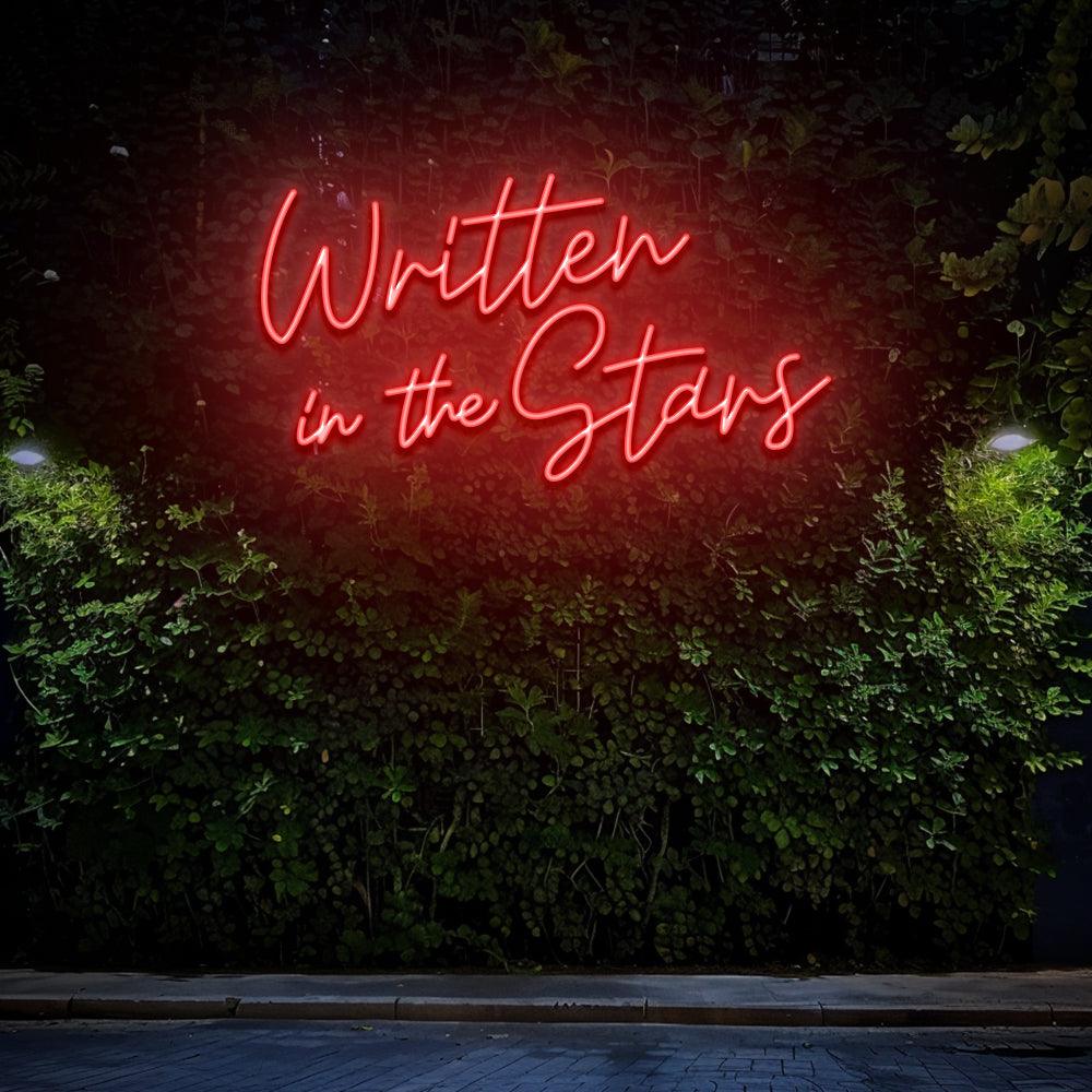 Written in the Stars neon lettering glowing red against a wall of green foliage