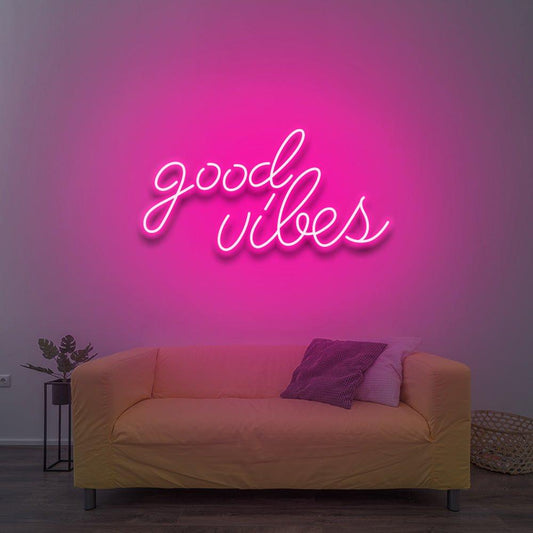 Pink Good Vibes LED neon sign glowing on a wall above a mustard-colored sofa